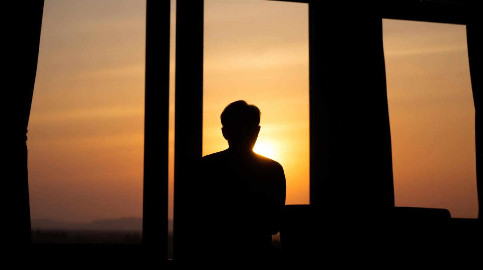Silhouet van een persoon bij een groot raam tijdens zonsondergang in een rustige stemming